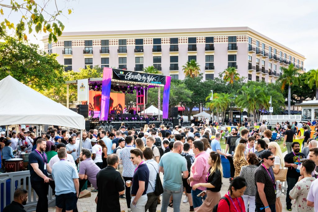 Un animado festival de música al aire libre con una gran multitud reunida alrededor de un escenario, disfrutando de las actuaciones bajo un cielo despejado