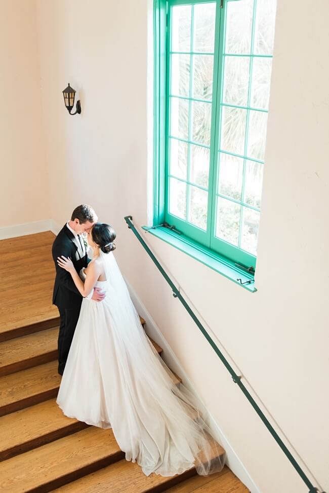 Bride and groom standing on a staircase in front of a teal window