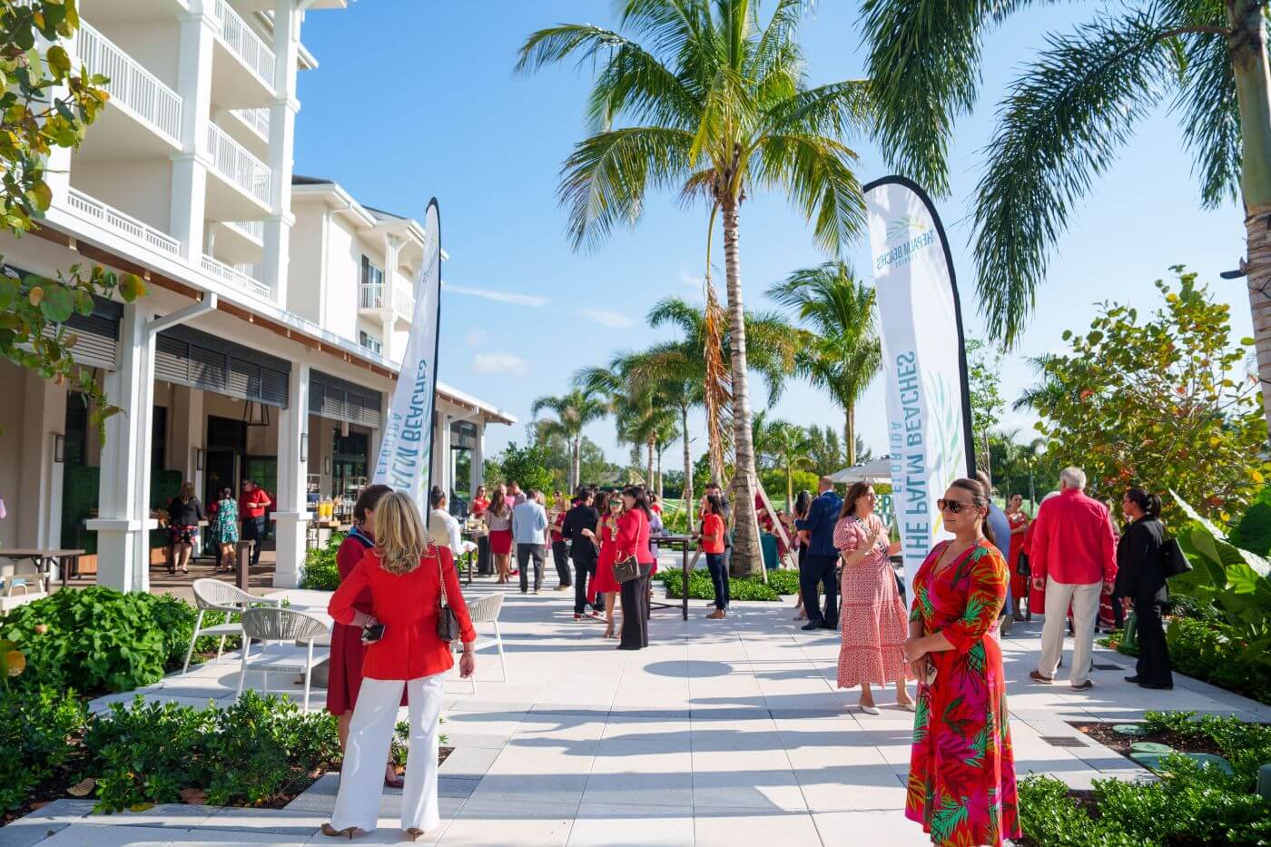 A lively outdoor social gathering at a tropical resort with guests mingling among palm trees and colorful banners