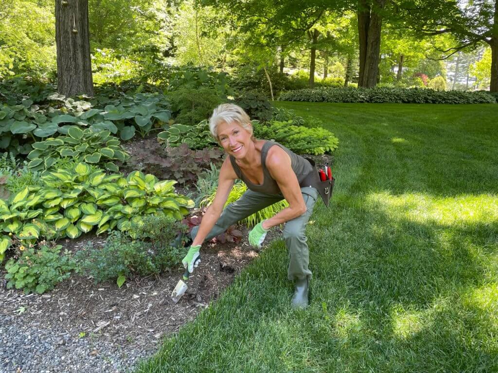 A woman in a garden, smiling as she plants a flower in a lush, green outdoor setting