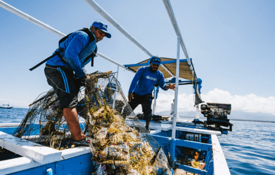 Two men on a boat pulling a net filled with ocean plastic waste
