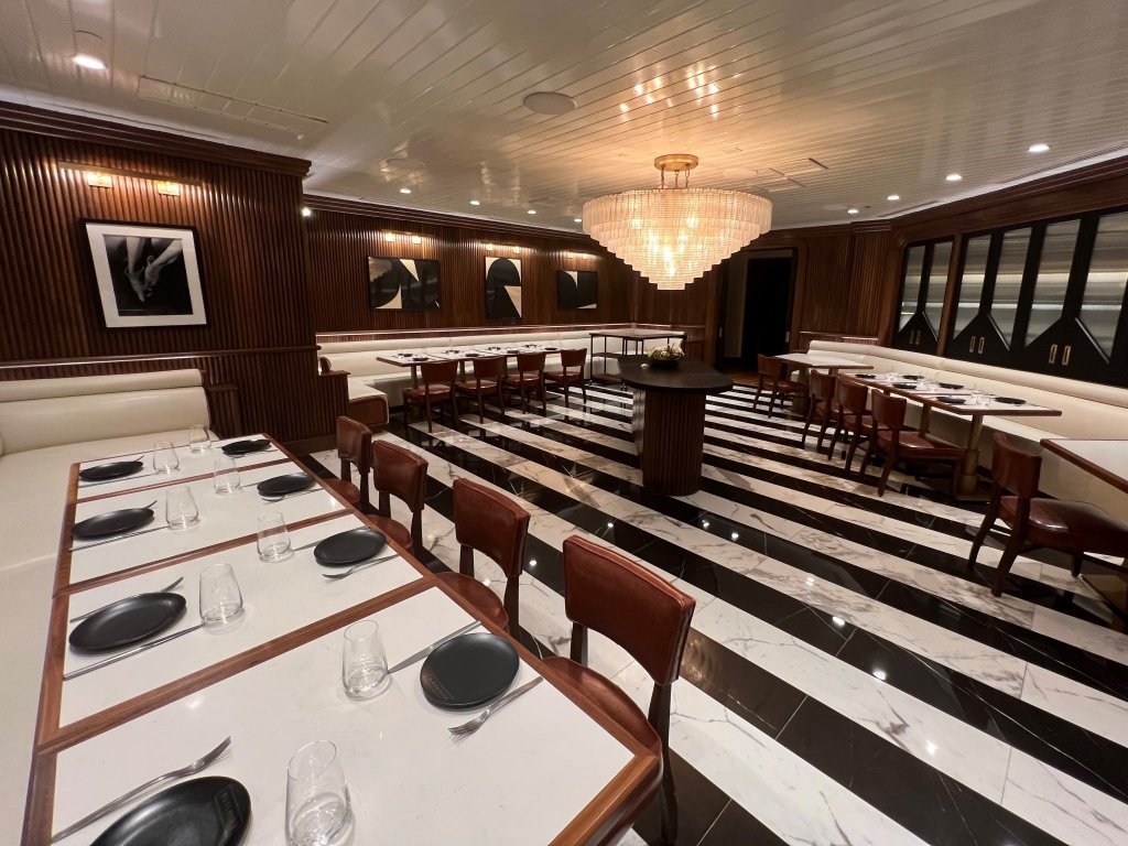 Salle à manger élégante avec sol en marbre noir et blanc, lambris en bois et lustres.