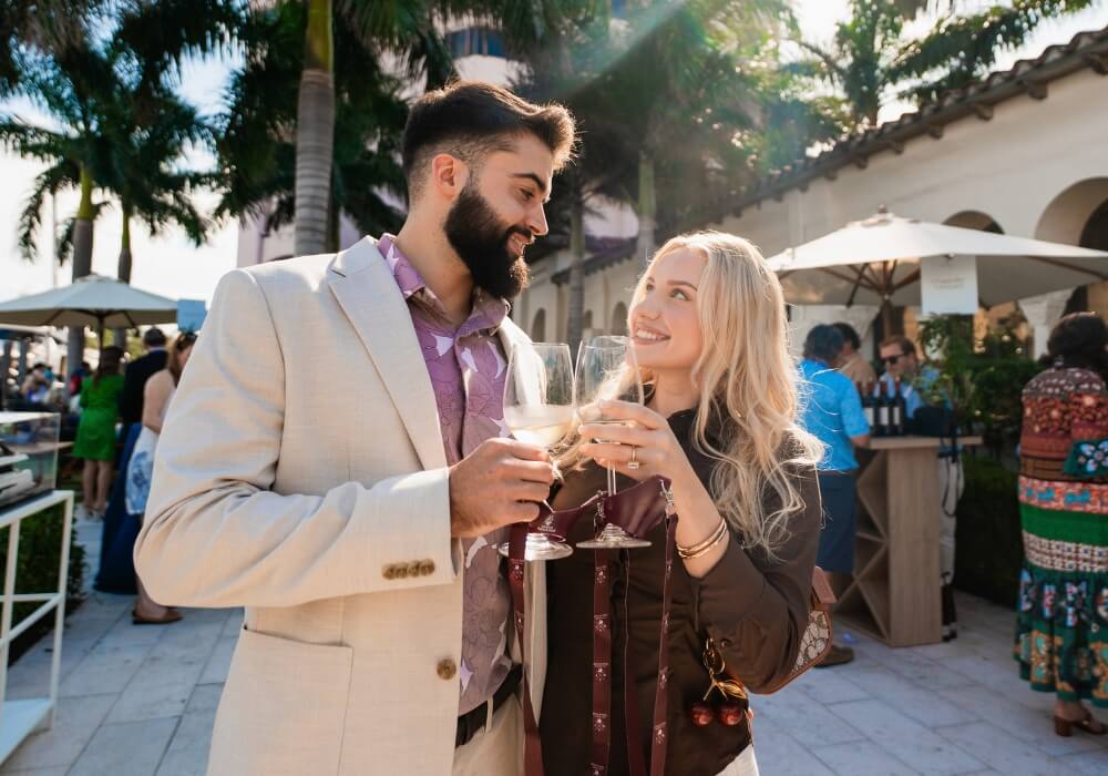 A couple smiling and clinking wine glasses at an outdoor social event