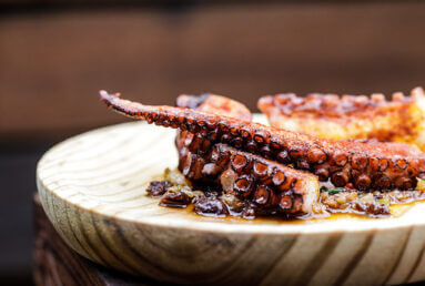 A plate of grilled octopus tentacles with a rich, dark sauce and garnished with herbs