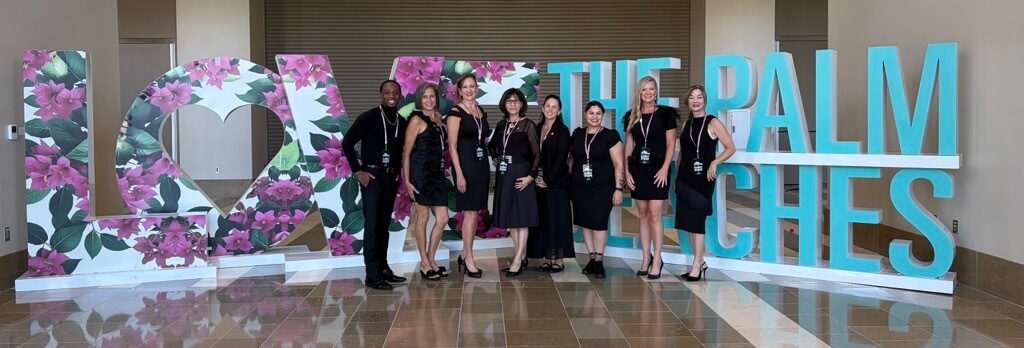 A group of nine people in black attire posing in front of large decorative letters