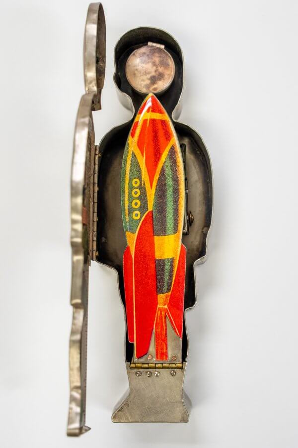 A vintage metal figurine of a person holding a colorful, retro-style rocket ship