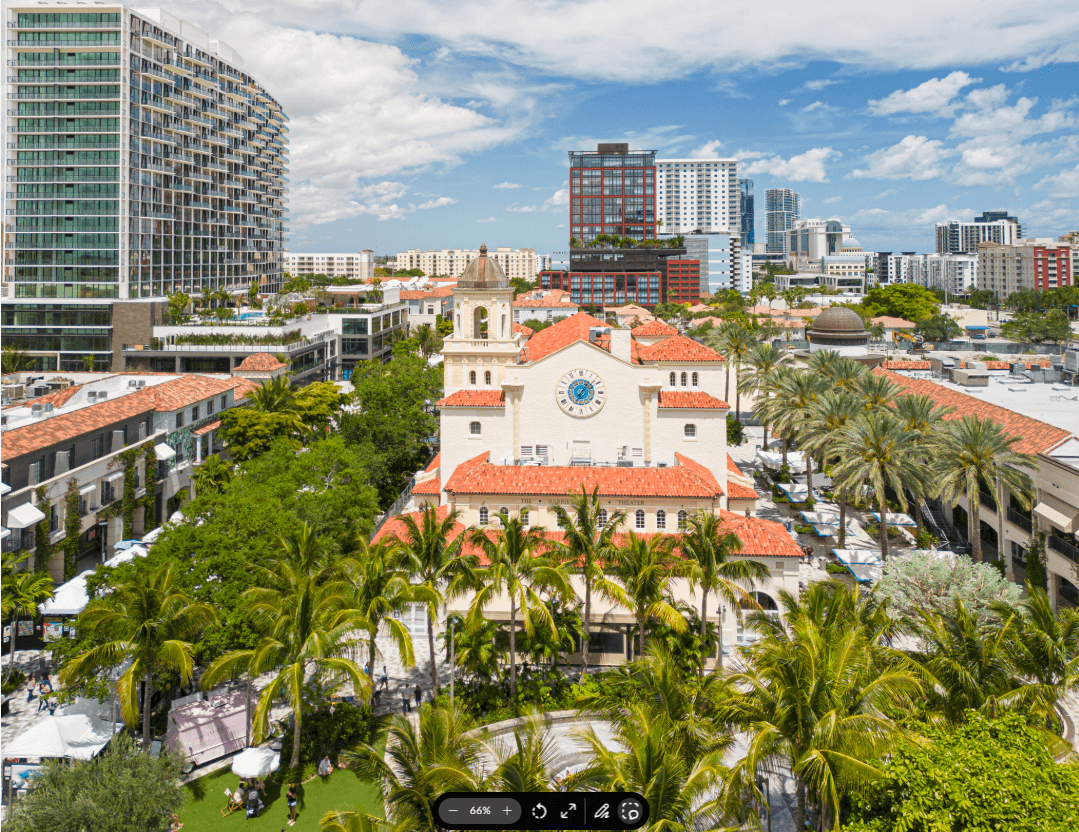 A vibrant cityscape featuring a prominent white church with a blue clock tower surrounded by lush palm trees and modern high-rise buildings under a clear blue sky
