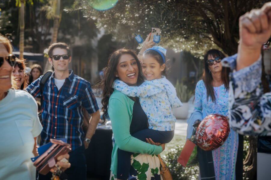 A joyful gathering of people in a park, with a woman holding a child and others celebrating around them