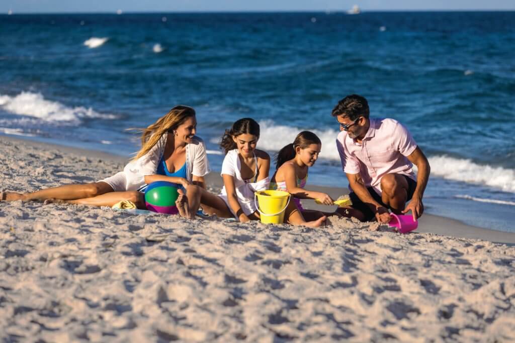 Une famille de quatre personnes profite d'une journée ensoleillée à la plage, en construisant des châteaux de sable et en jouant avec des jouets de plage colorés.
