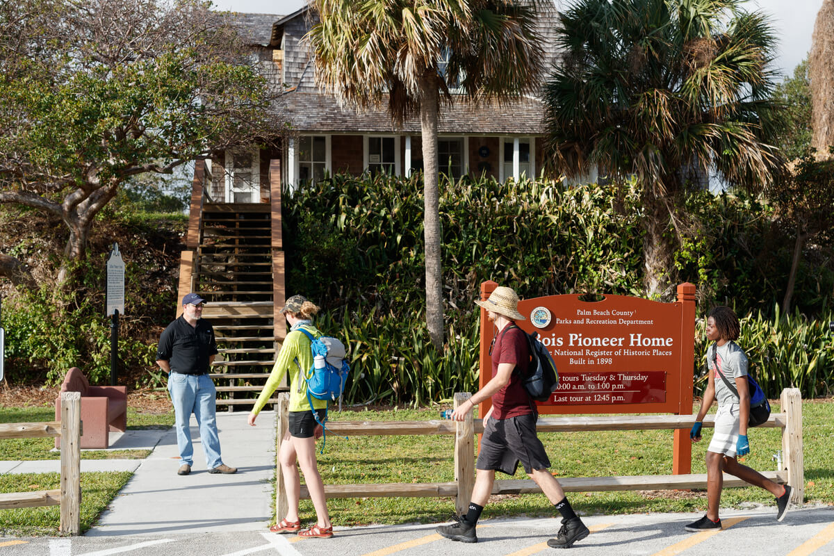 Visitors approach the entrance of the historic Pioneer Home, surrounded by lush greenery and palm trees