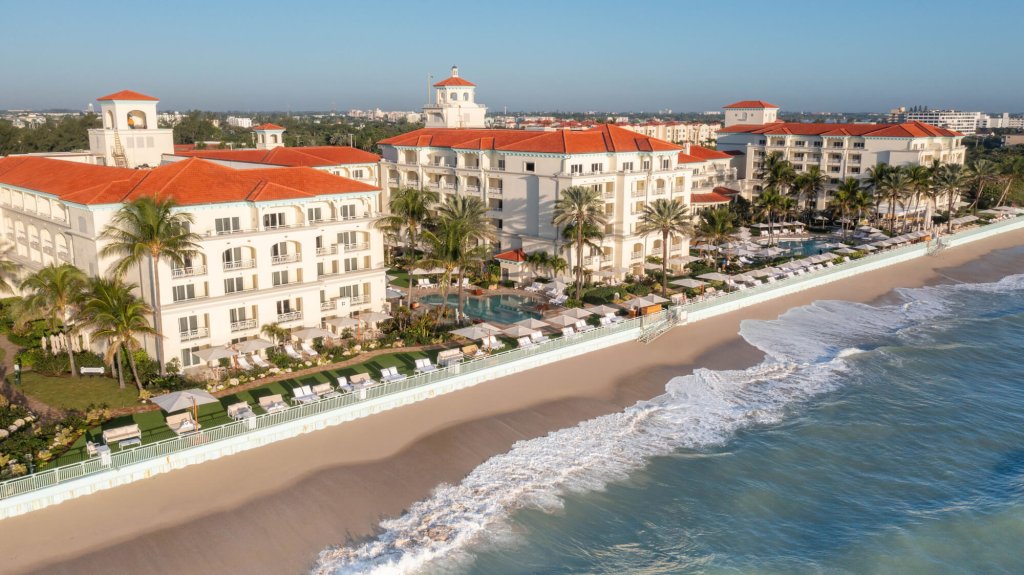 A luxurious beachfront resort with white buildings and red roofs, surrounded by palm trees and a pristine sandy beach