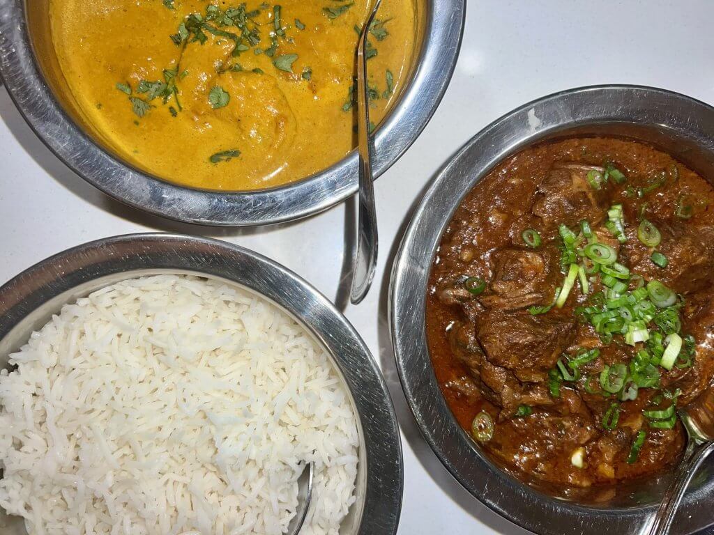 Three bowls of Indian cuisine: creamy yellow curry, rich brown curry with meat, and fluffy white rice
