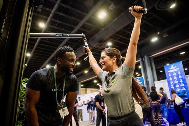 A man and woman are exercising together, with the woman enthusiastically lifting a weight above her head