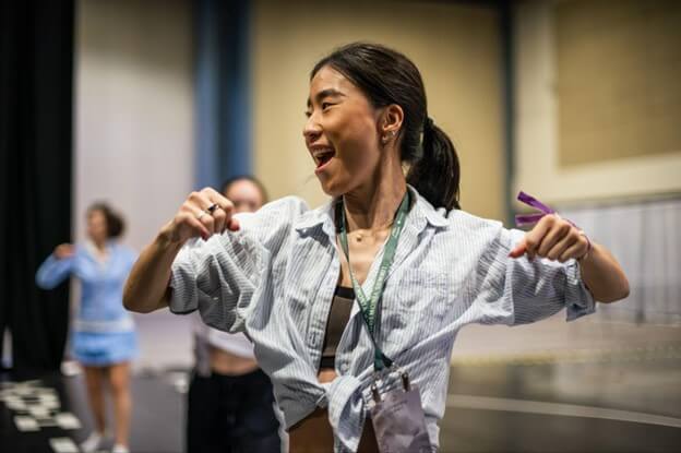 A young woman joyfully dances in a spacious indoor arena, her arms outstretched and a smile on her face