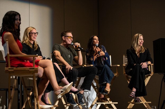 Five individuals are seated on stage in director's chairs, engaged in a panel discussion