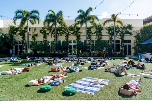 A group of people are relaxing on a grassy lawn surrounded by palm trees and a lush garden