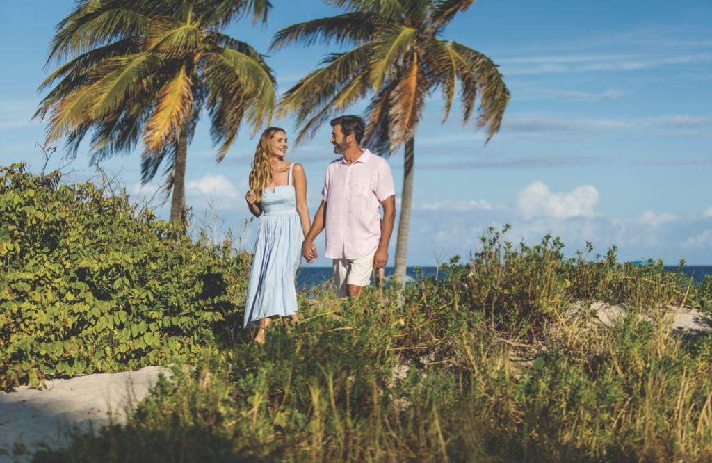 A couple walks hand-in-hand through a tropical landscape with palm trees