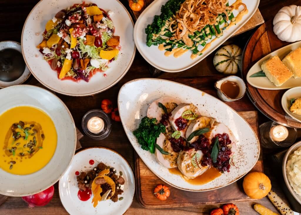 A festive autumn feast featuring a variety of dishes including roasted turkey, pumpkin soup, cornbread, mashed potatoes, and a colorful salad with seasonal fruits and vegetables