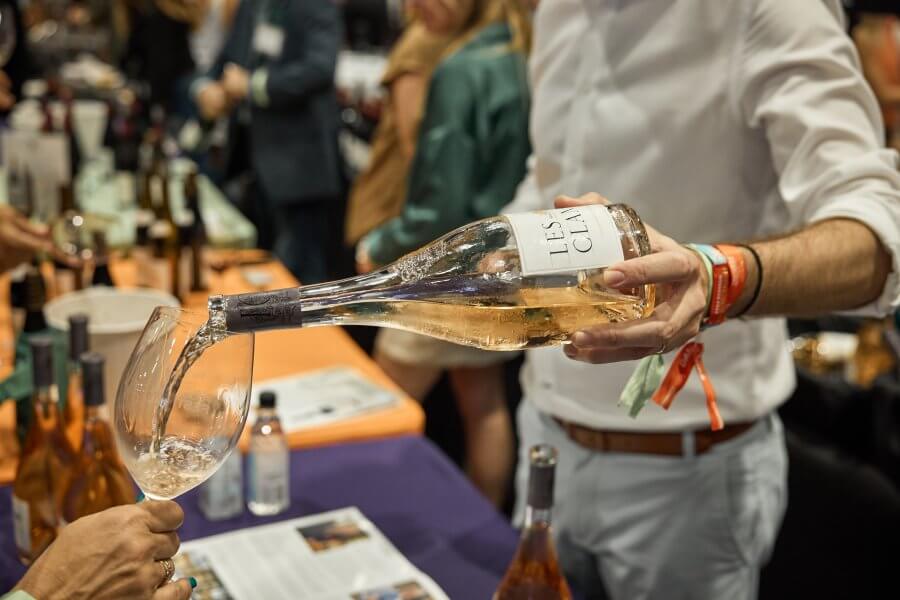 Un sommelier verse un vin rosé pâle d'une bouteille étiquetée 'Les Claux' dans un verre à vin lors d'une dégustation.
