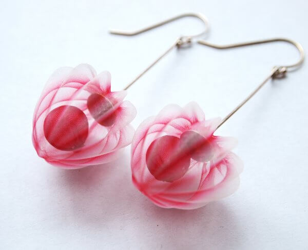 A pair of delicate earrings featuring translucent pink petals with red accents