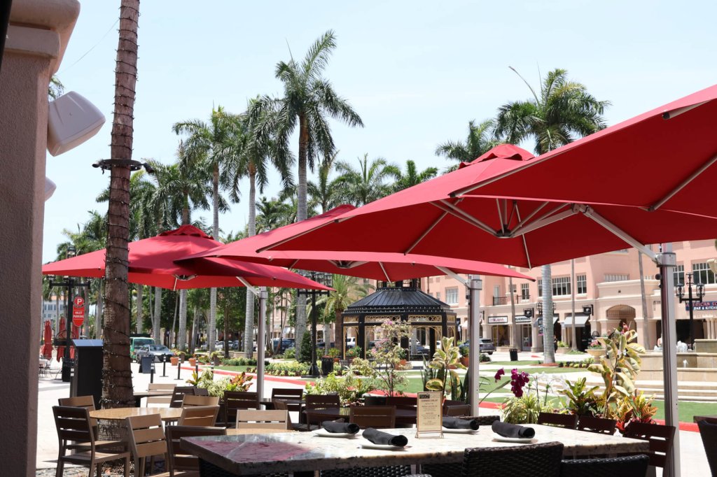 A vibrant outdoor dining area with red umbrellas and palm trees in a tropical setting