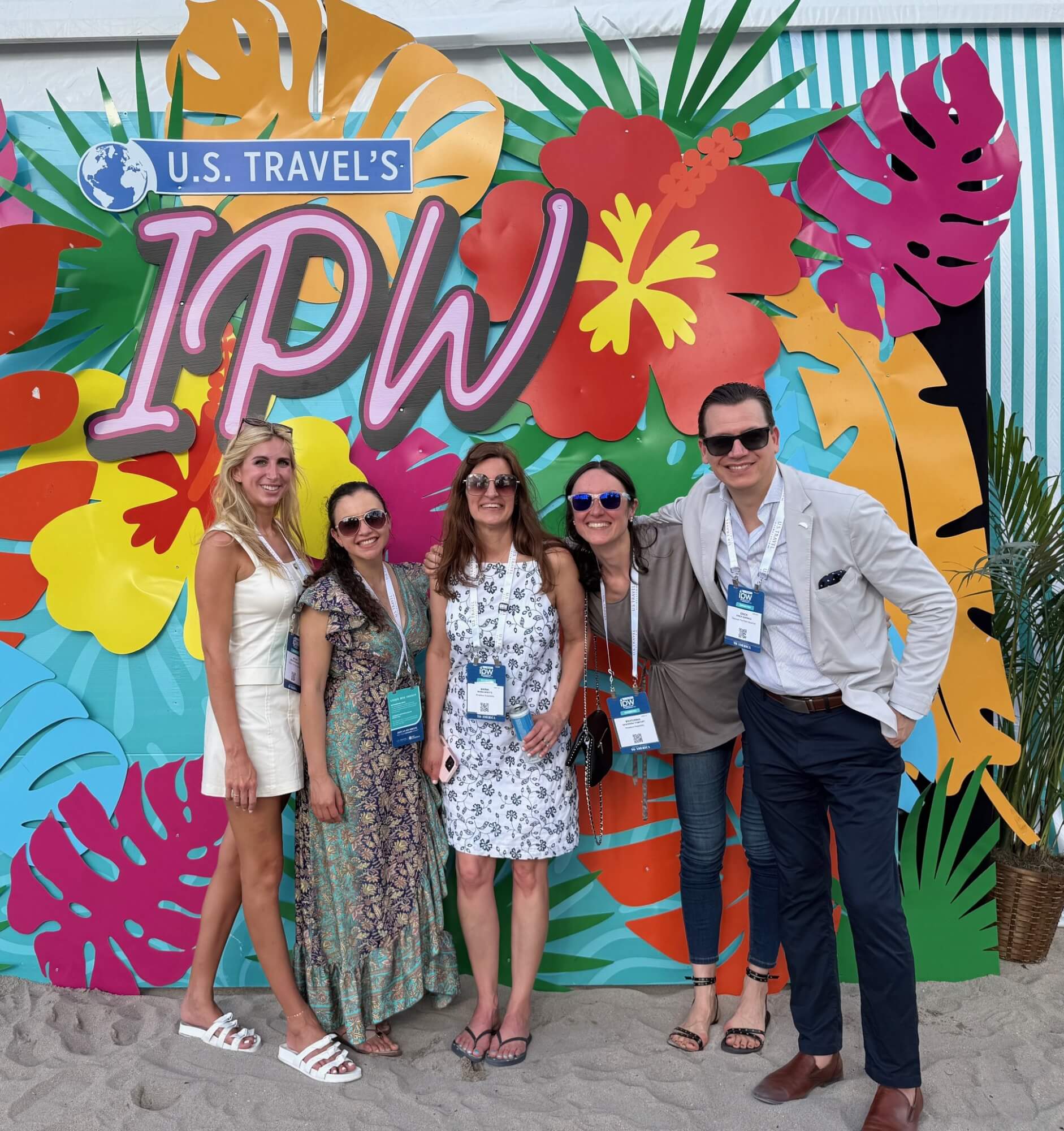 Five people posing for a photo in front of a colorful tropical IPW backdrop