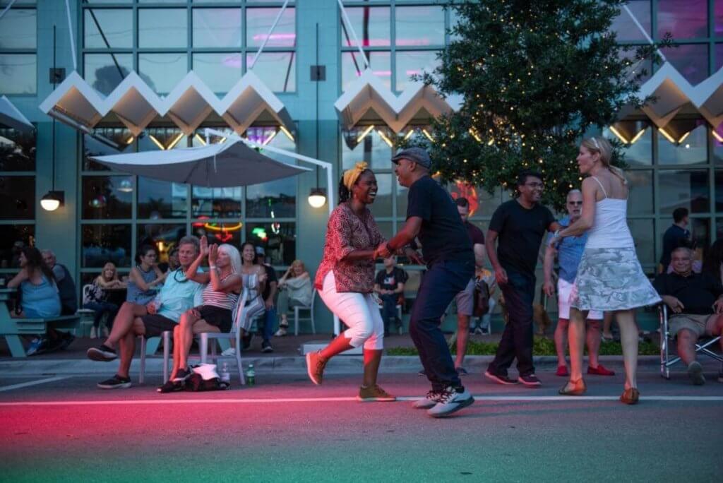 Uma animada festa de dança de rua com casais dançando sob luzes coloridas do lado de fora de um edifício moderno