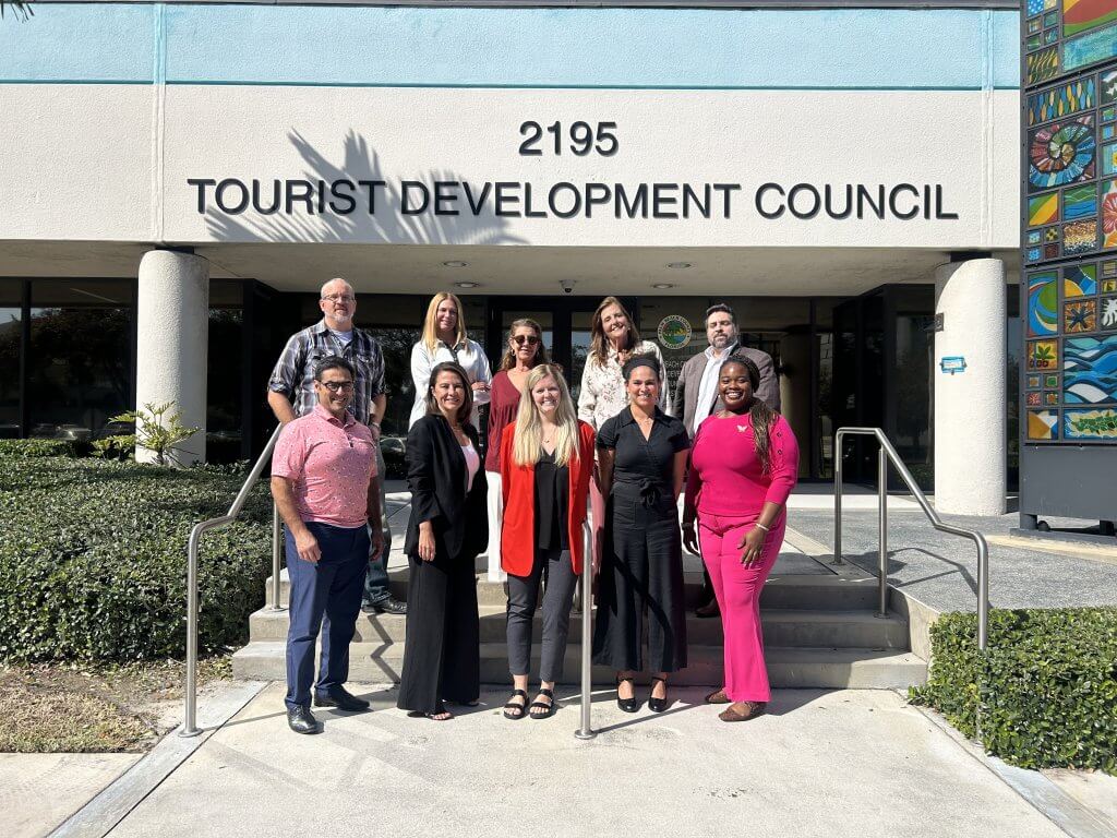 Un groupe diversifié de professionnels se tient devant le bâtiment du Conseil du développement touristique, souriant et posant pour une photo de groupe.