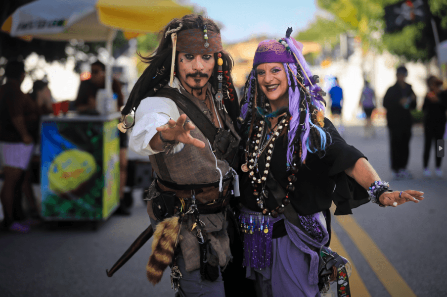 Two people dressed as pirates, one resembling Captain Jack Sparrow, strike a playful pose on a street filled with festival-goers