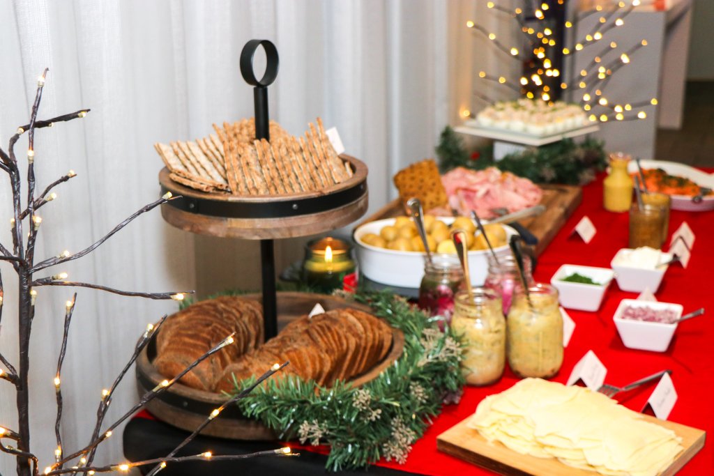 Ein weihnachtliches Buffet mit einer Vielzahl von Broten, Crackern, Fleisch, Käse und Gewürzen, dekoriert mit festlichen Lichtern und Grünzeug, um eine warme und einladende Atmosphäre zu schaffen.