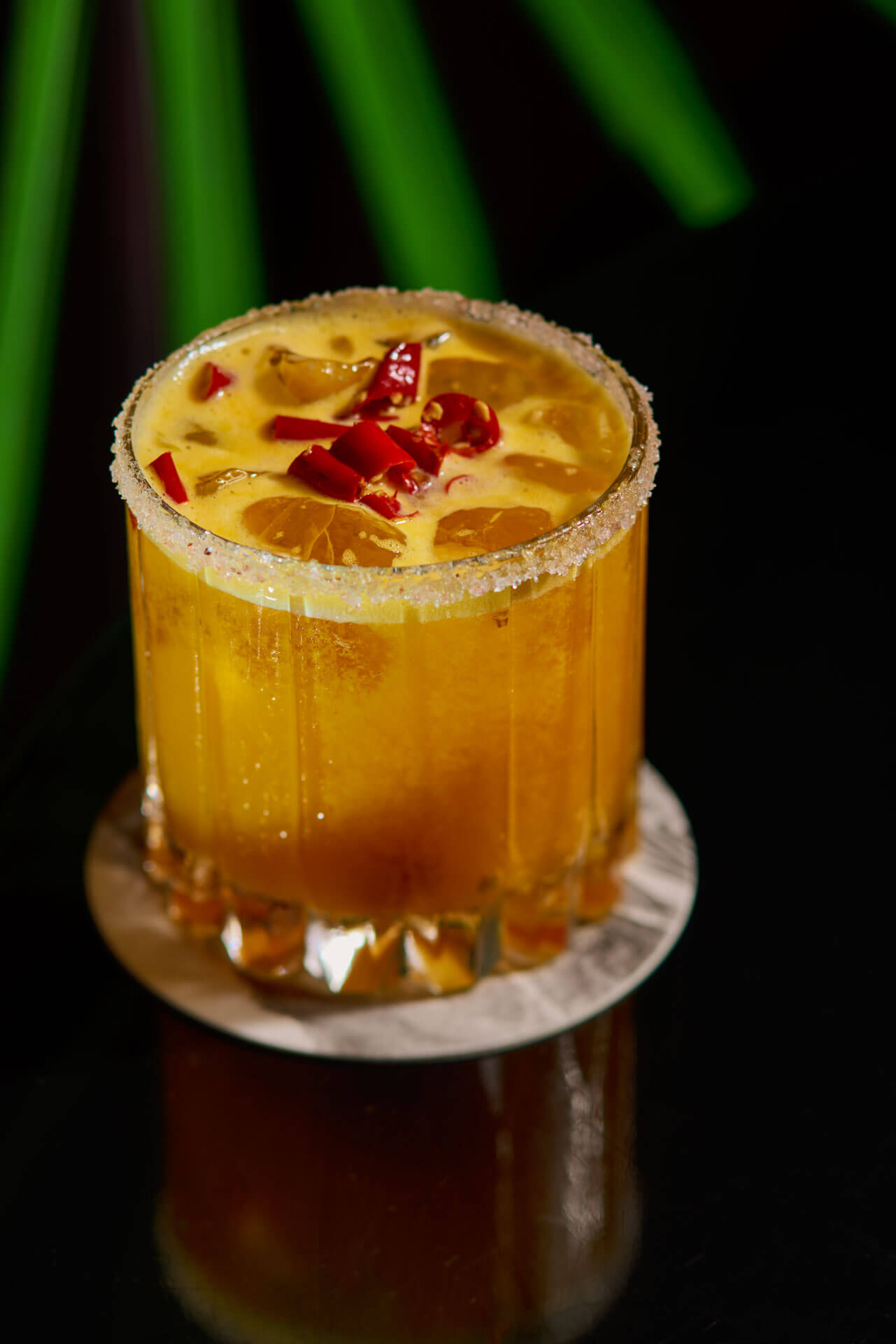 A spicy orange cocktail in a sugar-rimmed glass garnished with red chili slices