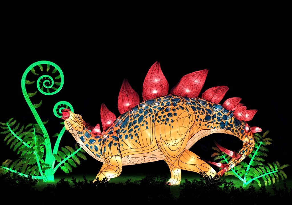 A vibrant, illuminated stegosaurus with red plates and a yellow body stands amidst glowing green ferns in a dark, prehistoric landscape