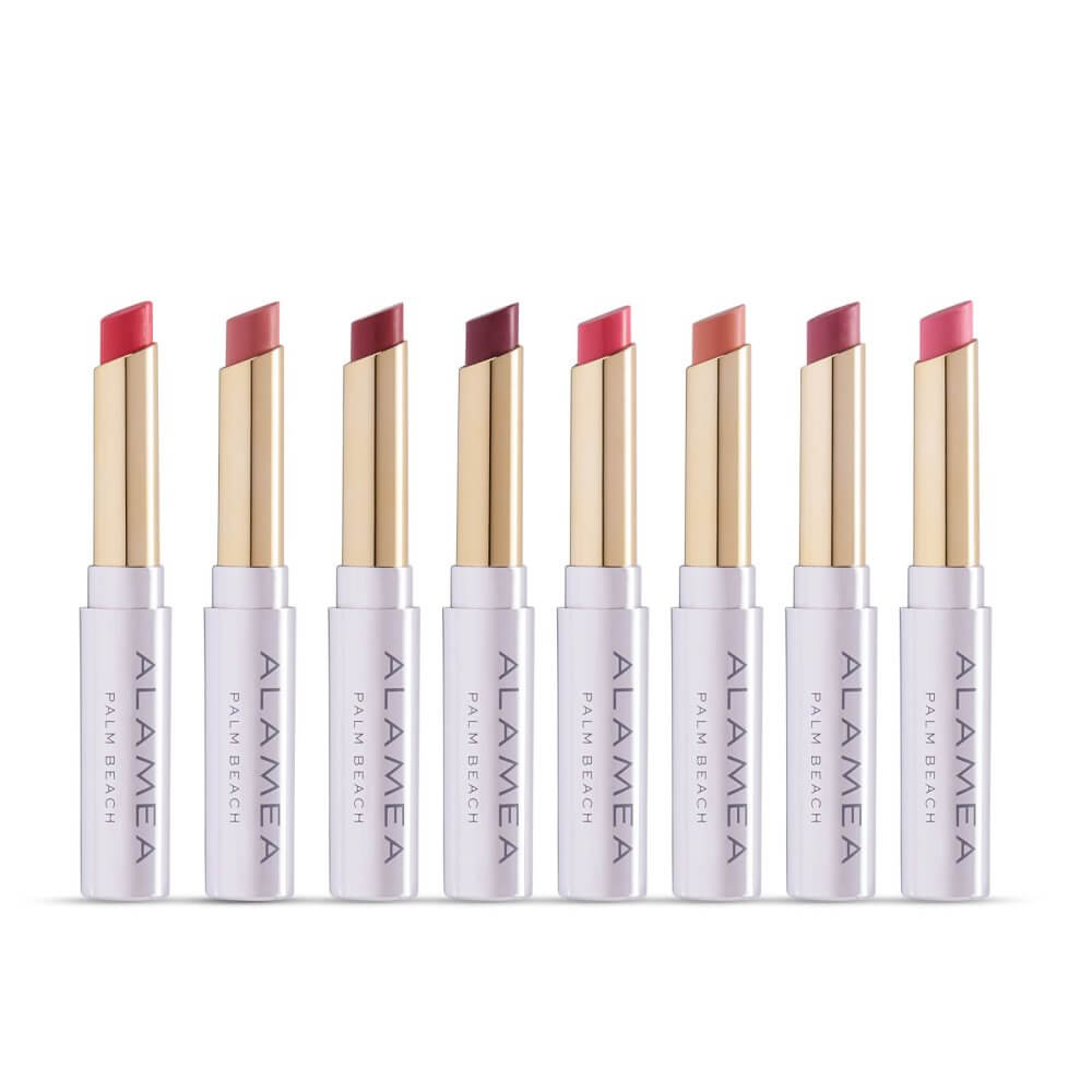 A row of eight Alamae Palm Beach lipsticks in various shades of red and pink, each with a gold-tipped cap