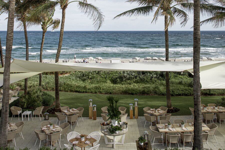 Un tranquilo restaurante frente al mar con toldos blancos, palmeras y mesas dispuestas para cenar con vistas al océano
