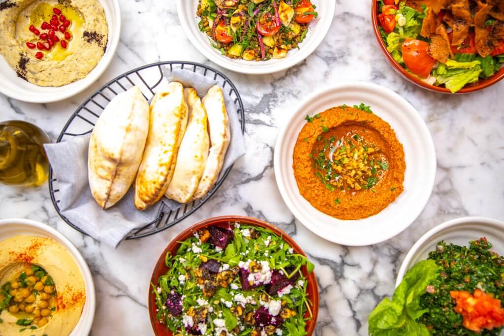 A variety of colorful and appetizing Middle Eastern dishes, including hummus, baba ganoush, tabbouleh, and falafel, are artfully arranged on a marble table