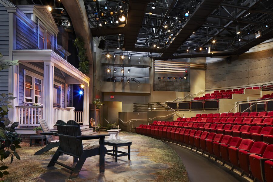 A theater stage set with a Victorian house and a garden, featuring red seats and a starry night sky backdrop