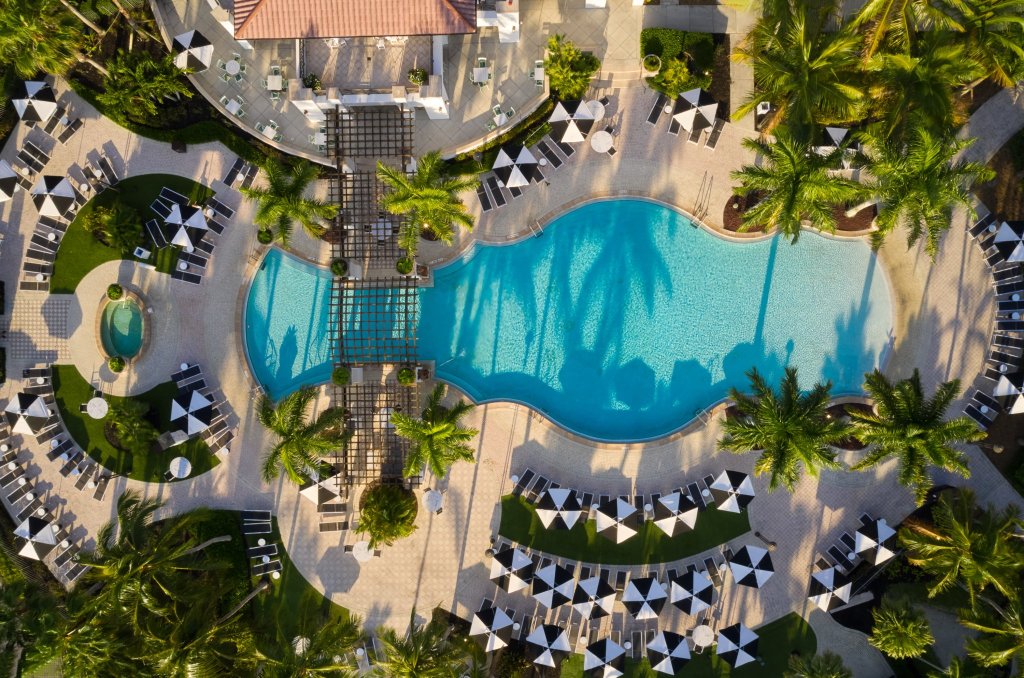 Luftaufnahme eines luxuriösen Resorts mit einem großen, nierenförmigen Swimmingpool, umgeben von Palmen und Liegestühlen