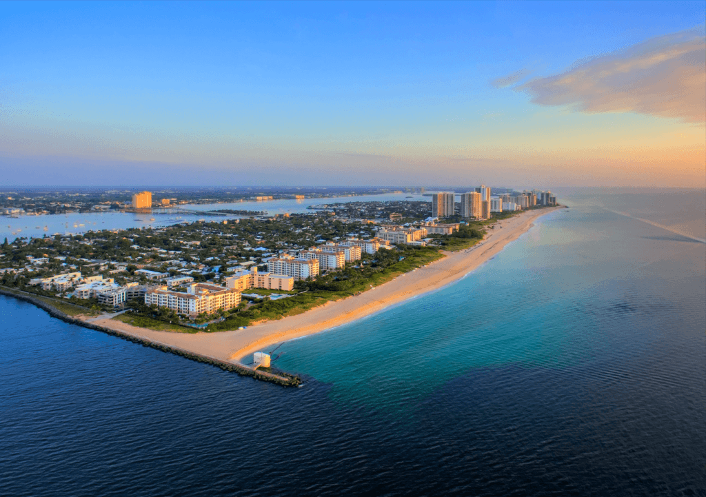 Vue aérienne d'une ville côtière dynamique avec une longue plage de sable et des eaux turquoises, bordée d'une ligne de gratte-ciel et d'une végétation luxuriante.