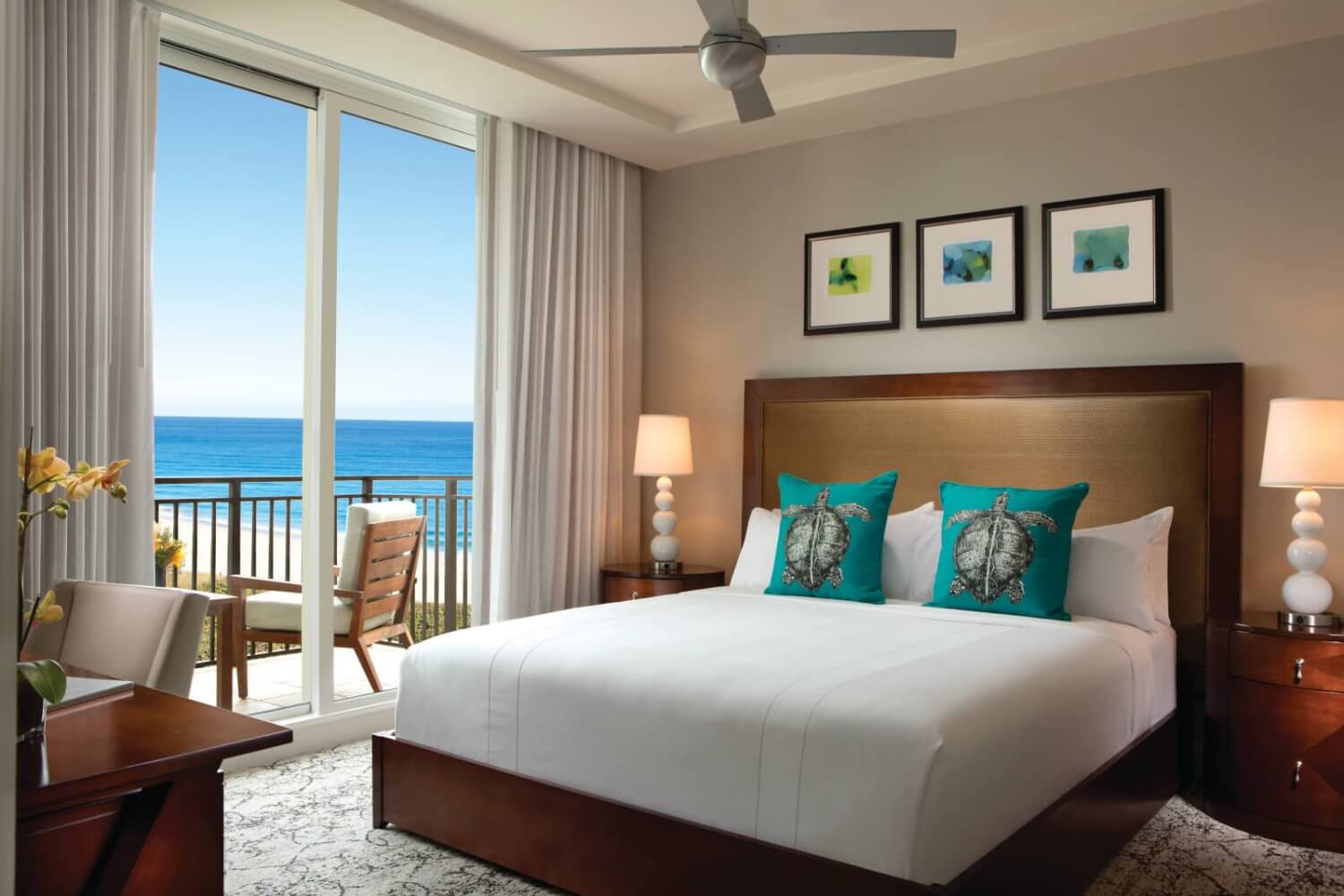 A serene beachfront hotel room with a king-size bed, turquoise accents, and a balcony overlooking the ocean