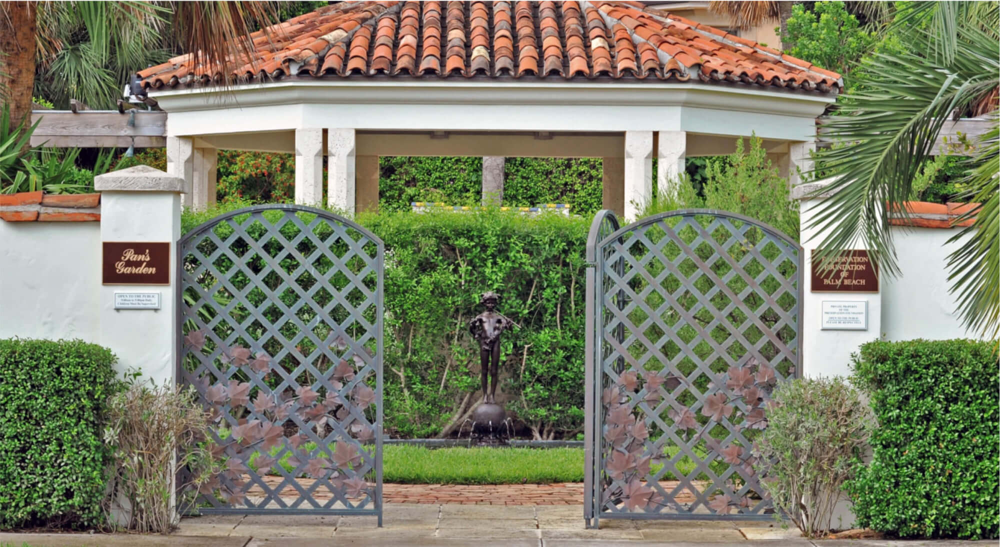 An ornate metal gate opens to a garden with a statue and gazebo