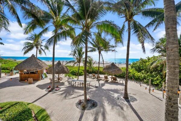 A tropical beach resort with thatched-roof huts, palm trees, and a clear blue ocean view