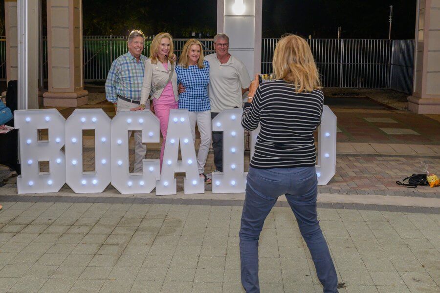 A group of six people posing for a photo in front of illuminated letter signs spelling out 'BOCA10' at night