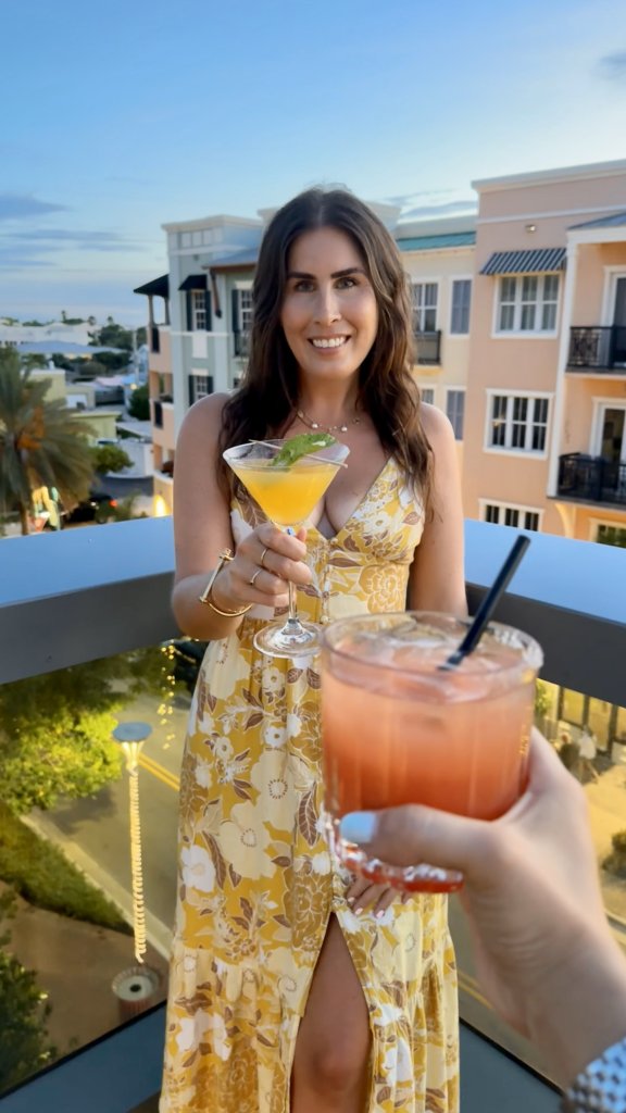 a woman standing on the rooftop with a cocktail