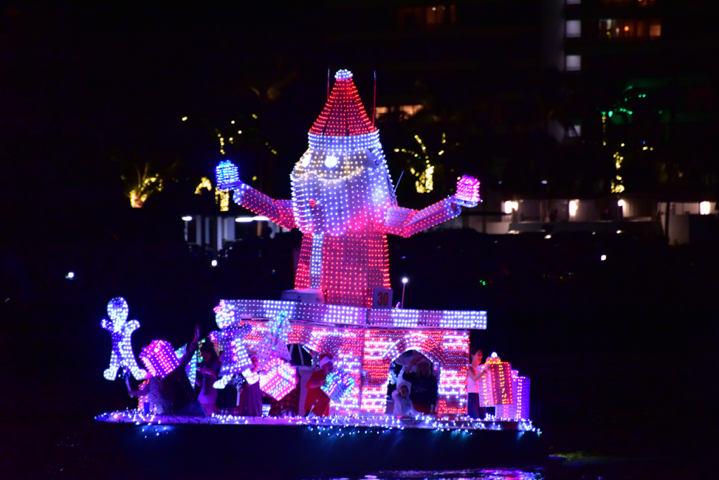 Desfile navideño en barco con una gran figura iluminada de Papá Noel con los brazos extendidos, rodeada de luces navideñas de colores.