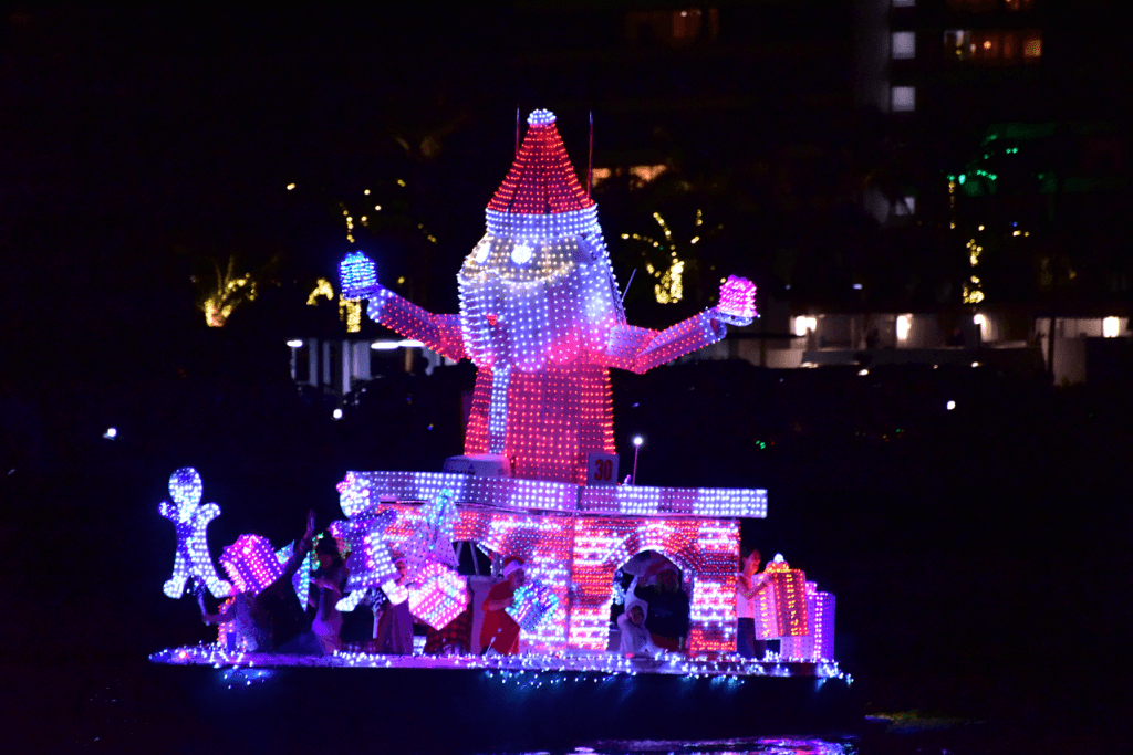 A festive boat parade featuring a giant illuminated Santa Claus and colorful Christmas decorations on a dark water body