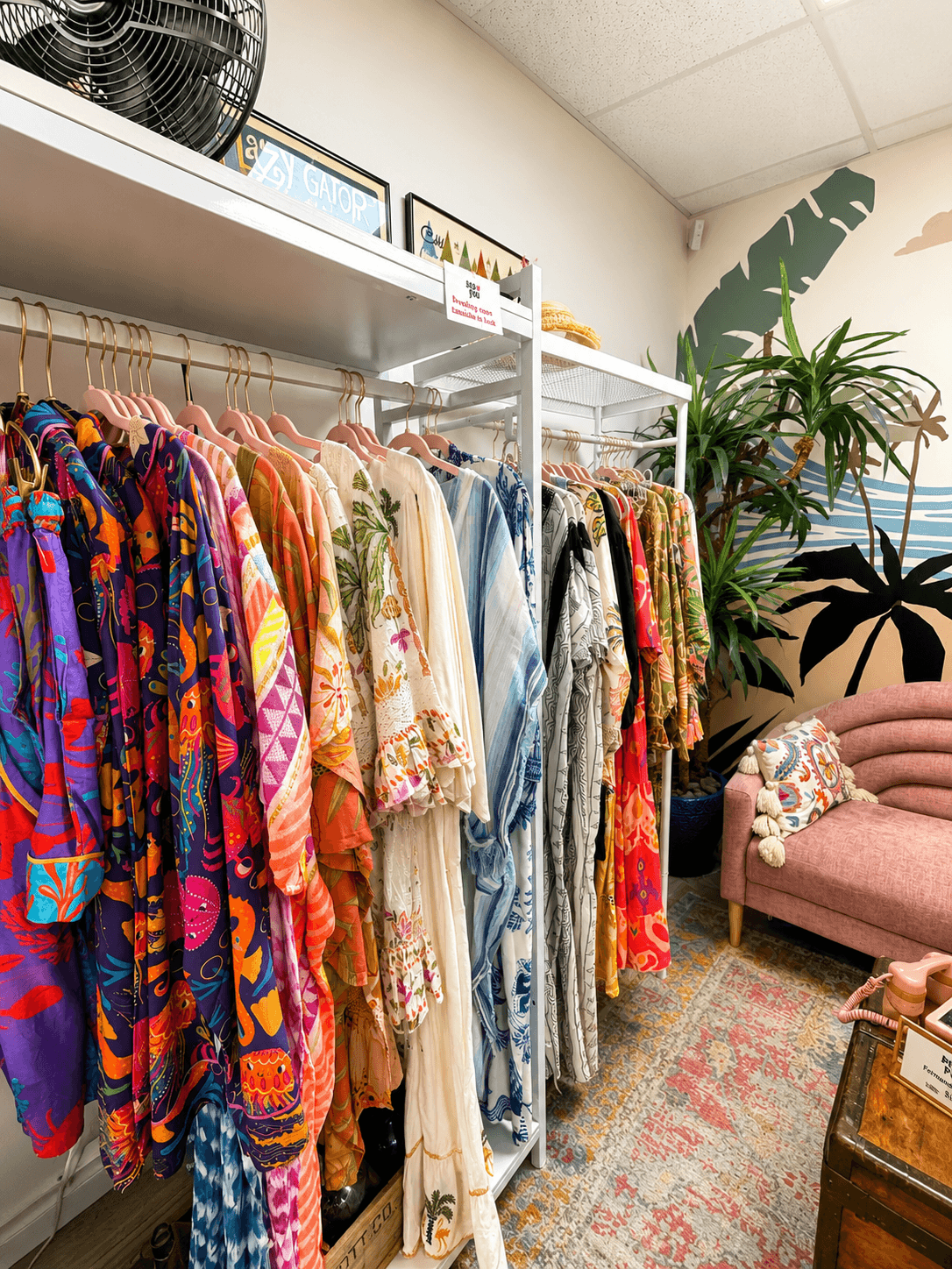 A vibrant clothing boutique with colorful garments hanging on racks, a pink sofa, and tropical wall art