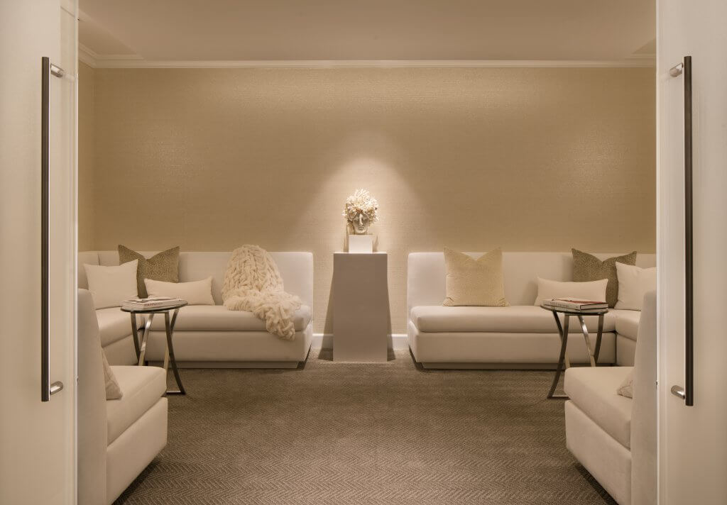 A serene and elegant sitting room with white sectional sofas, plush pillows, and a central pedestal featuring a decorative vase