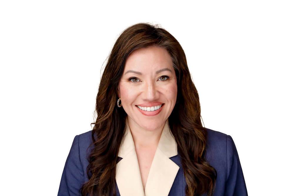 A smiling woman with long, dark hair wearing a blue suit jacket over a cream-colored blouse