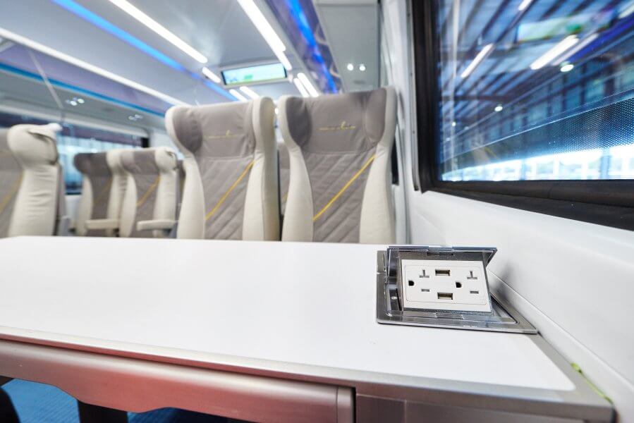 A modern train carriage interior with comfortable seats, a sleek table, and a built-in power outlet