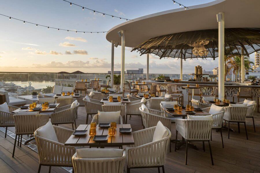 Un restaurante en la azotea con una marquesina curvada y guirnaldas de luces, con vistas al puerto deportivo al atardecer